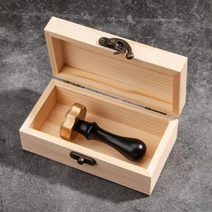 May include: A wooden box with a brass latch, open to reveal a black and gold wax seal stamp with a wooden handle.