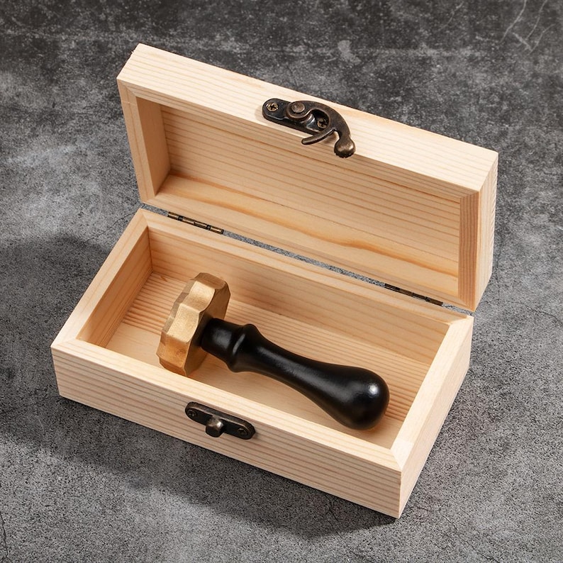 May include: A wooden box with a brass latch, open to reveal a black and gold wax seal stamp with a wooden handle.