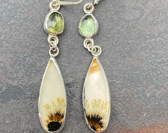 May include: A pair of silver dangle earrings with a teardrop-shaped agate stone and a smaller green gemstone. The agate stone has a white and brown dendritic pattern.