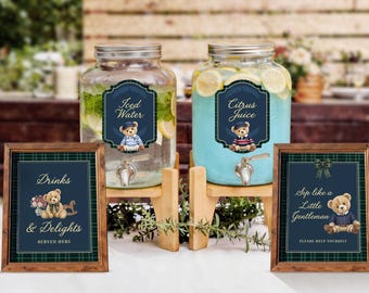 Op de afbeelding: Twee glazen drankdispensers op houten standaards met labels met een teddybeer. De ene bevat ijswater met citroenschijfjes, de andere citrussap. Twee ingelijste borden tonen de tekst Drinks & Delights en Sip like a Little Gentleman.