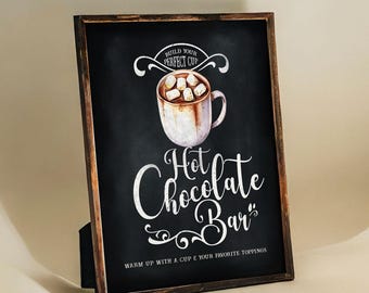 May include: A black chalkboard sign with white text that reads "Build Your Perfect Cup Hot Chocolate Bar" with a drawing of a mug of hot chocolate with marshmallows. The sign is framed in a dark wood frame.