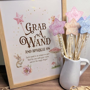 May include: A wooden framed print with the text "Grab a Wand and Sparkle On" and illustrations of a bunny, flowers, and mushrooms. Star-shaped wands with names like "Chloe" and "Adeline" are in a white jug.