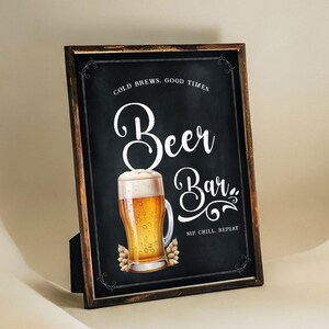 May include: A black chalkboard sign with white text that reads "Cold Brews, Good Times Beer Bar Sip, Chill, Repeat". A glass of beer with a white foam head is pictured in the center of the sign.
