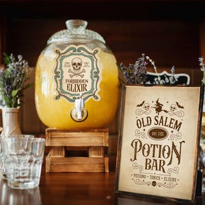 Puede incluir: Un gran dispensador de bebidas de vidrio lleno de líquido amarillo, etiquetado como "Forbidden Elixir". Un letrero de madera dice "Old Salem Potion Bar" con calaveras y murciélagos decorativos. La escena está preparada para una fiesta de Halloween o temática.