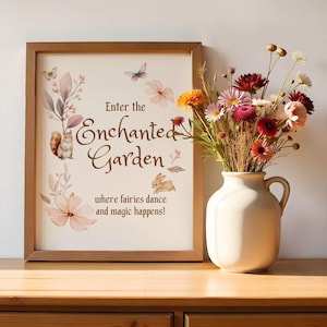 Puede incluir: Una impresión enmarcada con una ilustración de acuarela de una escena de jardín de ensueño. El texto dice "Entra en el Jardín Encantado donde las hadas bailan y la magia sucede!"