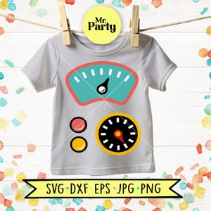 May include: A light grey short-sleeve t-shirt featuring a graphic print of a teal speedometer, a black circular gauge with a red needle, and two small circles in red and yellow. The shirt is displayed hanging from a wooden clothespin.
