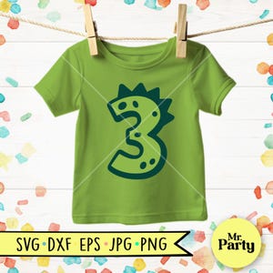 Pu&ograve; includere: Una maglietta verde lime per bambini con un disegno del numero 3 verde scuro. Il numero 3 ha l'aspetto di un dinosauro con punte e punti. La maglietta &egrave; appesa a un filo per stendere con mollette di legno. La parte inferiore dell'immagine contiene il testo "SVG DXF EPS JPG PNG".