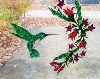 May include: A green hummingbird with a long beak flies towards a floral design with red and pink flowers. The flowers are painted on a glass surface.