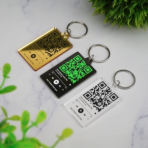 Könnte beinhalten: Drei Schlüsselanhänger mit unterschiedlichen Hintergrundfarben. Jeder Schlüsselanhänger hat einen QR-Code und den Text "Your Custom Song Title", "Your Custom Text Here" und "Your Custom Song Title".