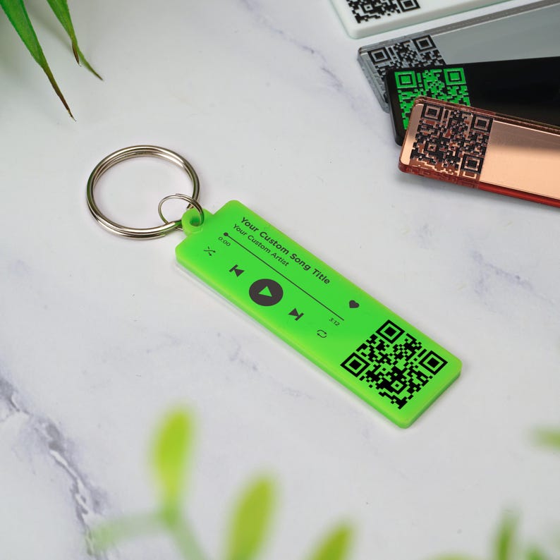 May include: A bright green keychain with a black and white QR code, play button, and the text "Your Custom Song Title" and "Your Custom Artist".