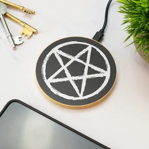 May include: A black and white wireless charging pad with a pentagram design. The charging pad is round and has a wooden rim.