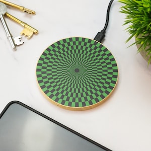 May include: A round wireless charging pad with a black and green chequered pattern. The pattern creates a swirling optical illusion.