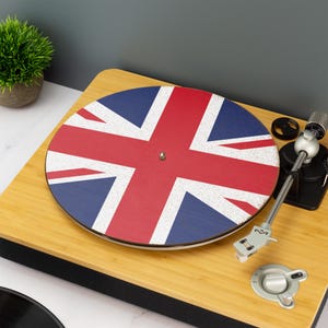 Może przedstawiać: Drewniany gramofon z motywem Union Jack na talerzu. Talerz ma czerwono-biało-niebieski wzór flagi. Gramofon jest wykonany z jasnego drewna i ma srebrne ramię.