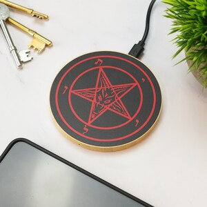 May include: A black and red wireless charging pad with a pentagram and a goat's head design. The charging pad is round and has a gold rim.