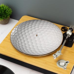 Może przedstawiać: Biała ceramiczna mata na talerz gramofonowy z fakturowanym wzorem w kształcie plastra miodu. Mata znajduje się na drewnianym gramofonie.
