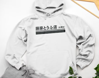 Può includere: Una felpa con cappuccio bianca con una stampa grafica nera che dice "藤原とうふ店 (豆腐屋)" in giapponese.