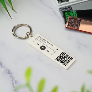 May include: White keychain with a black and white QR code, play button, and the text "Your Custom Song Title" and "Your Custom Artist".