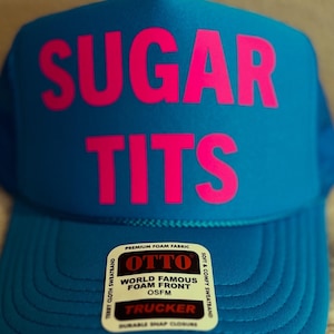 May include: A blue trucker hat with a pink "SUGAR TITS" logo on the front. The hat has a black and white label that reads "OTTO WORLD FAMOUS FOAM FRONT OSFM TRUCKER DURABLE SNAP CLOSURE".
