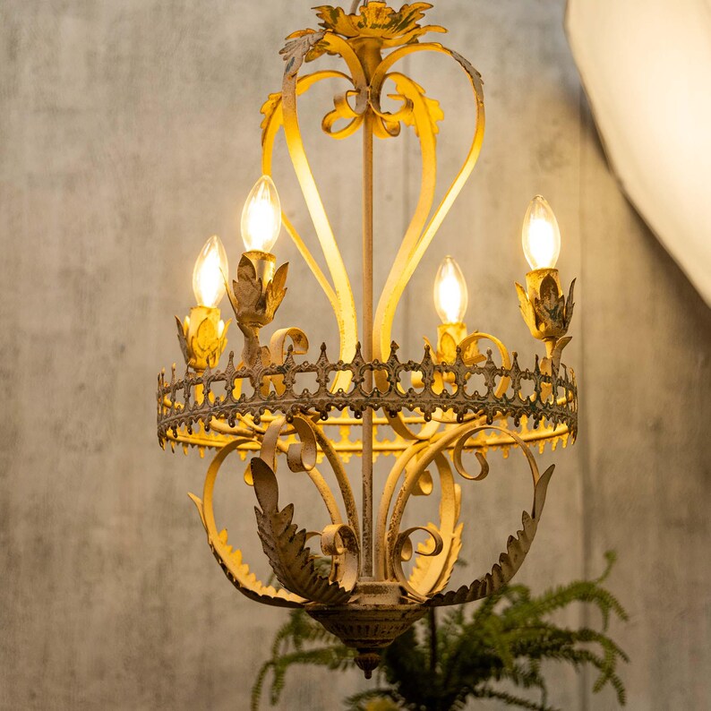 May include: A gold metal chandelier with a distressed white finish and ornate detailing. The chandelier has five lights and is hanging from a ceiling.