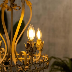 May include: A white metal chandelier with a decorative design and three lit bulbs.