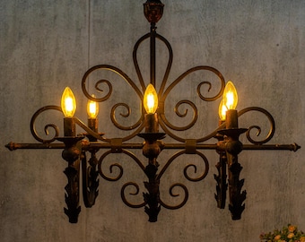 May include: A black wrought iron chandelier with five lights. The chandelier has a decorative scroll design and is lit with warm white bulbs.