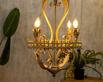 May include: A white and gold metal chandelier with a scrolled design and three light bulbs. The chandelier has a distressed finish and is hanging from a ceiling.