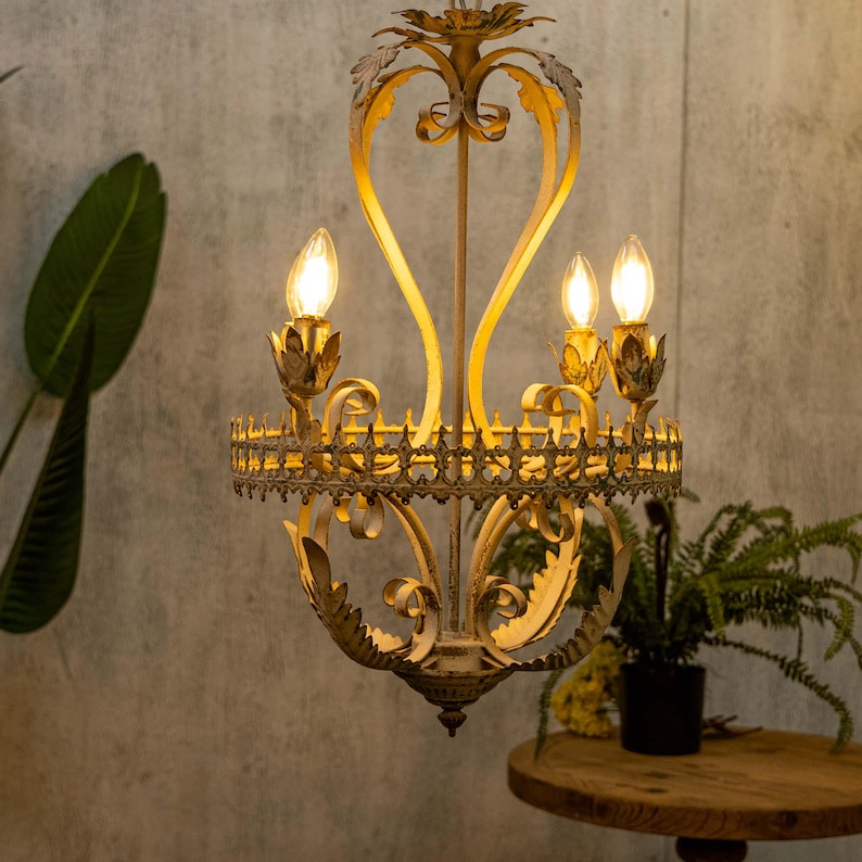 May include: A white and gold metal chandelier with a scrolled design and three light bulbs. The chandelier has a distressed finish and is hanging from a ceiling.