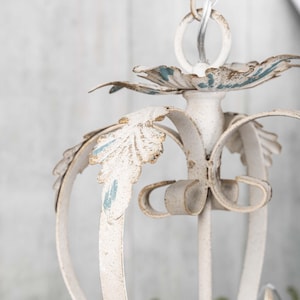 May include: White metal chandelier with a distressed finish and blue accents. The chandelier has a floral design with leaves and scrolls.