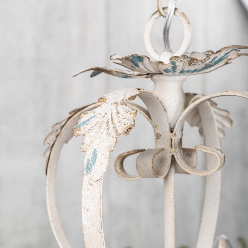 May include: White metal chandelier with a distressed finish and blue accents. The chandelier has a floral design with leaves and scrolls.