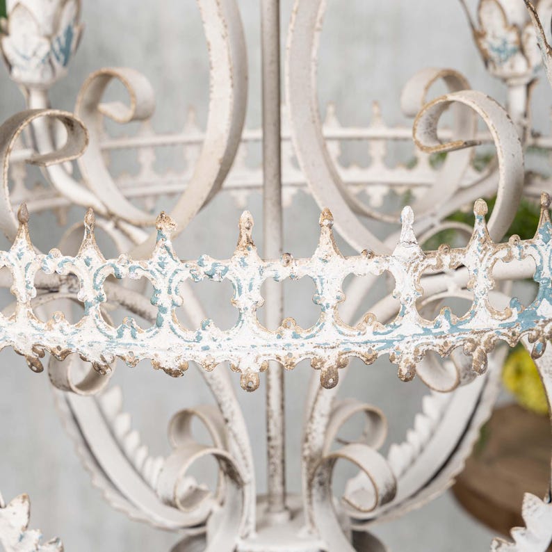 May include: A white metal chandelier with a decorative, ornate design. The chandelier has a distressed finish with blue accents.