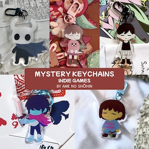 Könnte beinhalten: Eine Sammlung von Acryl-Schlüsselanhängern mit Charakteren aus Indie-Spielen. Die Schlüsselanhänger haben verschiedene Designs, darunter ein Ritter, eine Figur in einem rosa Kleid, eine Figur in einem schwarzen Kleid, eine Figur mit einem Schwert und eine Figur in einem blauen Hemd.