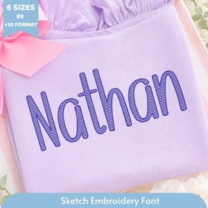 May include: A light purple fabric featuring the embroidered name Nathan in a dark blue sketch-style font. A light blue tag in the top left corner displays the text 6 SIZES BX +10 FORMAT, and a light blue banner at the bottom reads Sketch Embroidery Font.