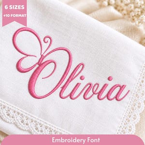 May include: A white fabric piece featuring pink machine embroidery of the name Olivia, where the letter O is stylized as a butterfly. The fabric has a decorative lace border. A pink banner at the top left reads 6 SIZES +10 FORMAT.