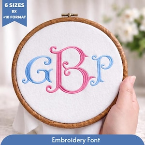 Op de afbeelding: Een borduurring met witte stof met de geborduurde letters "GBJ" in blauw en roze. De houten ring houdt de stof strak. De tekst "Embroidery Font" staat onderaan.