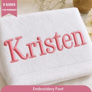 Puede incluir: Una toalla de algodón blanca con el nombre Kristen bordado en hilo rosa en el centro. La toalla tiene una superficie de tela texturizada con un detalle de borde decorativo en la parte inferior. Una banda rosa en la esquina muestra 5 SIZES +10 FORMAT.