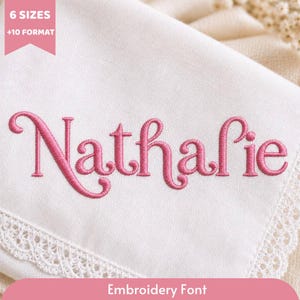 Puede incluir: Una pieza de tela blanca con el nombre Nathalie bordado en letra cursiva rosa. La tela tiene un borde decorativo de encaje blanco. Una pancarta rosa en la esquina superior izquierda muestra el texto 6 SIZES +10 FORMAT.