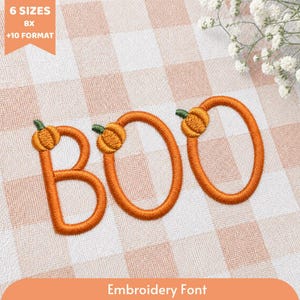 May include: An embroidery design featuring the word BOO, where each letter is formed by an orange stitched outline topped with a small green-stemmed pumpkin. The text 6 SIZES BX +10 FORMAT and Embroidery Font are visible on the fabric.