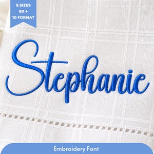 May include: Close-up of white fabric with the name "Stephanie" embroidered in blue cursive script. The fabric has a subtle grid pattern and a decorative border. Text at the top reads "6 SIZES BX + 10 FORMAT". The text at the bottom reads "Embroidery Font".