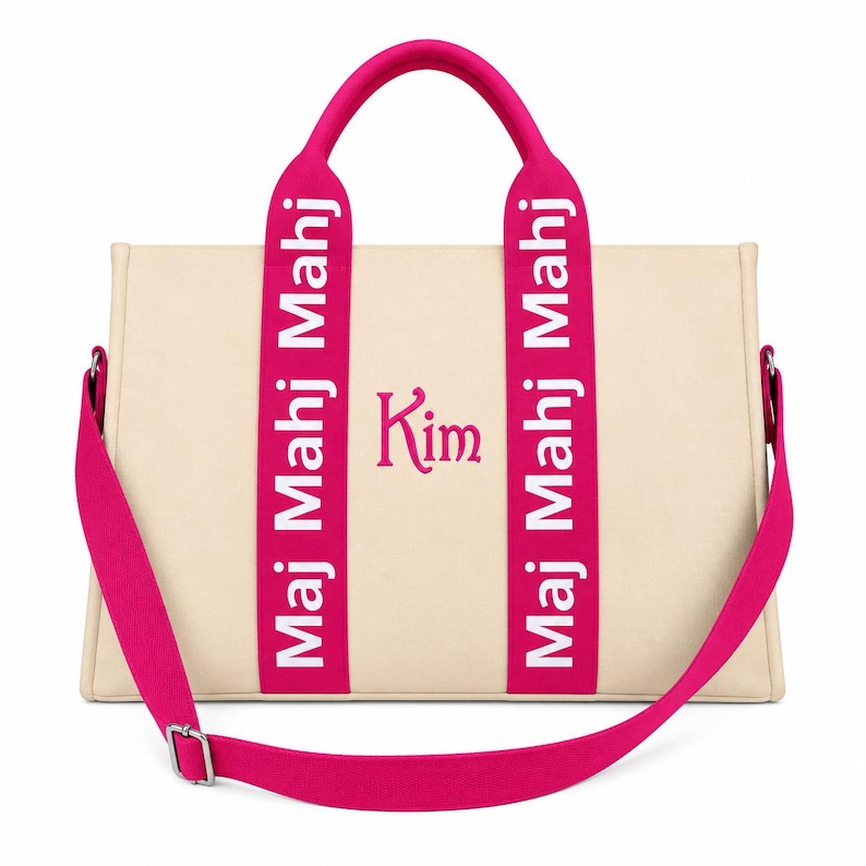 May include: A beige tote bag with bright pink handles and a matching detachable shoulder strap. The pink handles feature the white text "Maj Mahj Mahj" repeated vertically. The center of the bag displays the name "Kim" in pink script lettering.