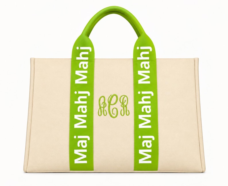 May include: A beige tote bag featuring two lime green vertical straps with the white text "Maj Mahj Mahj" printed on each. The center of the bag displays a lime green embroidered monogram with the letters "ACR" in a cursive script font.