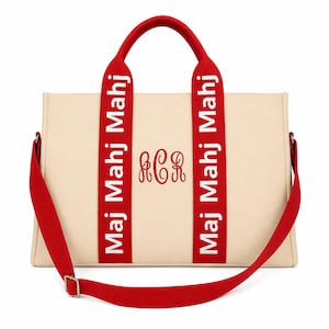 May include: A beige canvas tote bag featuring two red vertical straps with the white text "Maj Mahj Mahj" printed on each. The center of the bag displays a red embroidered monogram with the letters "ACR" in a cursive script font.