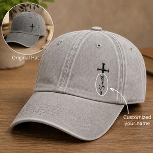 May include: A grey baseball cap with a distressed finish featuring an embroidered black cross design on the front panel. The design includes the text Smith written vertically along the cross. An inset shows the original hat with only a cross.