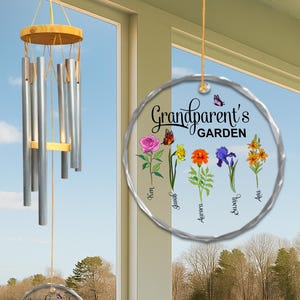 May include: A wind chime with silver tubes and a wooden top hangs near a window. A clear, circular ornament with the text "Grandparent's GARDEN" and floral illustrations is suspended nearby. The ornament features names like Ken, Jonah, Aurora, Susan, and Ava.