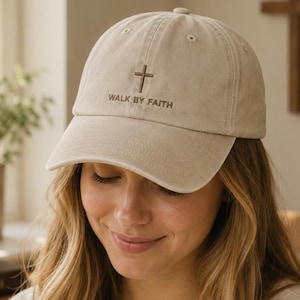 May include: A beige baseball cap featuring an embroidered brown cross and the text "WALK BY FAITH" centered on the front panel. The cap has a structured crown, a curved brim, and stitched eyelets for ventilation, providing a classic look.