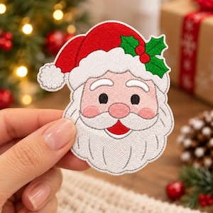 May include: An embroidered patch featuring the face of Santa Claus wearing a red hat with a white pom-pom and trim, accented by green holly leaves and red berries. The design includes a white beard, mustache, and eyebrows.