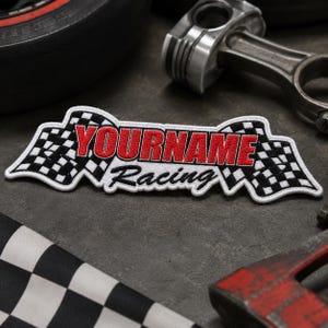 May include: A rectangular embroidered patch featuring a black and white checkered flag design on both ends. The text YOURNAME is stitched in bold red capital letters, with the word Racing embroidered in black cursive script underneath the red text.