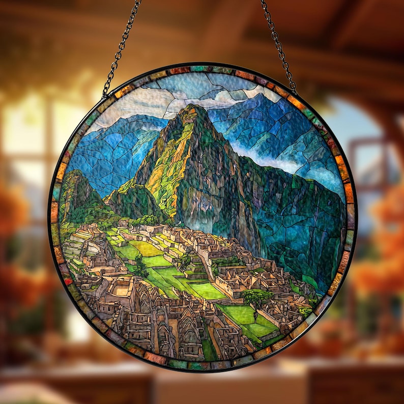 May include: Round stained glass window depicting the ancient city of Machu Picchu. The artwork features a detailed landscape with green mountains, blue skies, and the stone structures of the city. The window is framed in black and hangs from a chain.