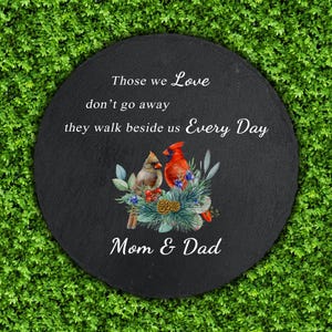 May include: A round, black stone garden marker with the text "Those we Love don't go away they walk beside us Every Day" and "Mom & Dad". It features a watercolor image of two cardinals and floral accents.