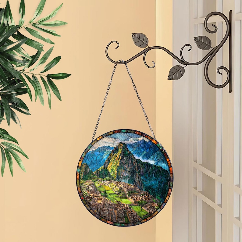 May include: A round stained glass panel depicting the Machu Picchu mountain landscape. The panel is framed with a mosaic border and hangs from a decorative metal chain. The panel is suspended from a decorative metal wall bracket with leaf accents.