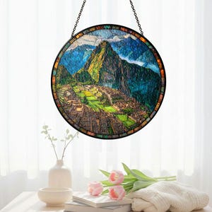 May include: Round stained glass window depicting Machu Picchu, with a black metal frame and hanging chain. The artwork features a colorful landscape of mountains, buildings, and sky. The window is displayed in front of a white curtain.